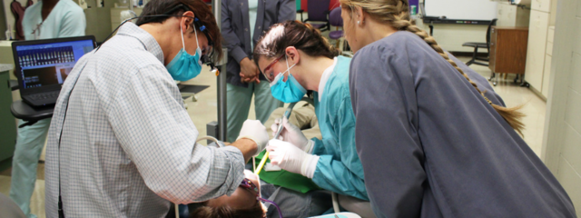 Man and Two Women Hover Over Patient in Chair Man and Two Women Hover Over Patient in Chair