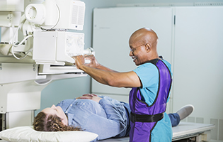 Older bald black man setting up a machine to x-ray a white woman with brown hair laying on a table Older bald black man setting up a machine to x-ray a white woman with brown hair laying on a table