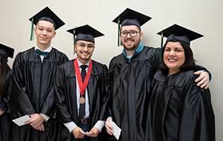 Group of four graduates smiling in their caps and gowns Group of four graduates smiling in their caps and gowns