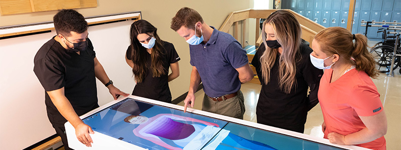 Table Showing the Anatomy of a Human Body With Students Standing Around It. Table Showing the Anatomy of a Human Body With Students Standing Around It.